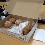 An open box of donuts on a wood conference room table next to plugs and office chairs
