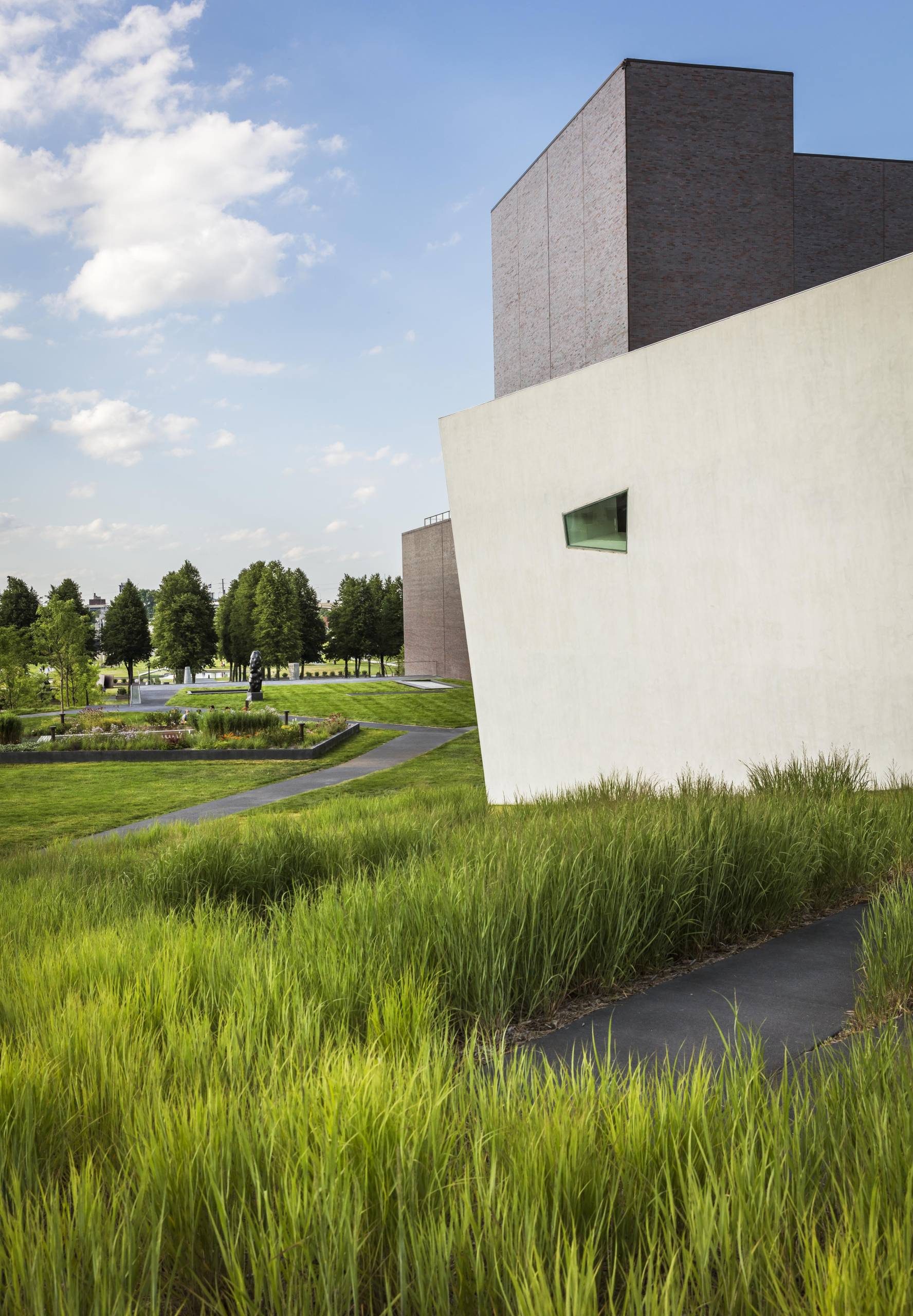 A large grey building next to a smaller white building with a rhombus shaped window next to grass and trees on a sunny day