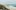 britt-gaiser-eNzBGf4fucc-unsplash A sandy beach with small white waves and grass patch and wood fence behind it