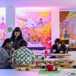 Adults looking down and smiling at a table with art supplies and colorful cartoons on the wall