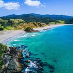 A high angle view of a coastline with crystal blue waters and lush green hills beyond the sandy beach
