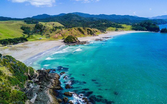 A high angle view of a coastline with crystal blue waters and lush green hills beyond the sandy beach