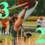 A person with a ponytail and glasses waving a multicolored ribbon in front of an outdoor scultpure at the Walker Art Center. With green text reding 