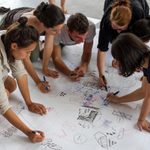 A group of adults write on a large piece on paper on the floor.