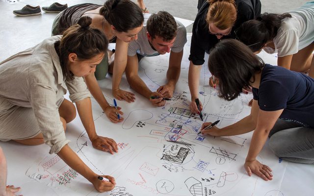 A group of adults write on a large piece on paper on the floor.