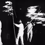 People in all white holding sticks that emit light, moving the sticks around in a live art installation at the Walker Art Center