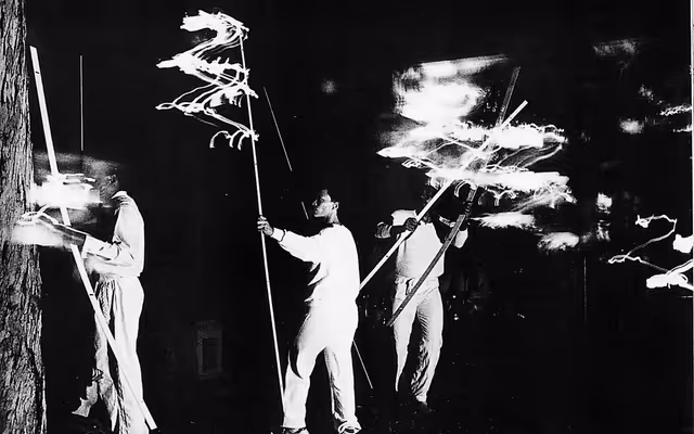 People in all white holding sticks that emit light, moving the sticks around in a live art installation at the Walker Art Center