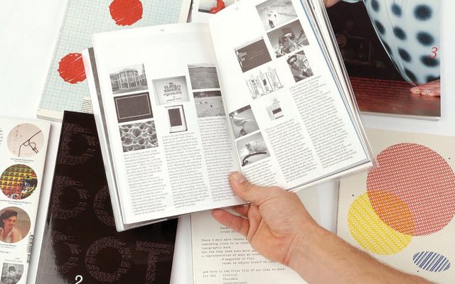 A right hand holding open a book with black and white pictures with text below, over several colored books.