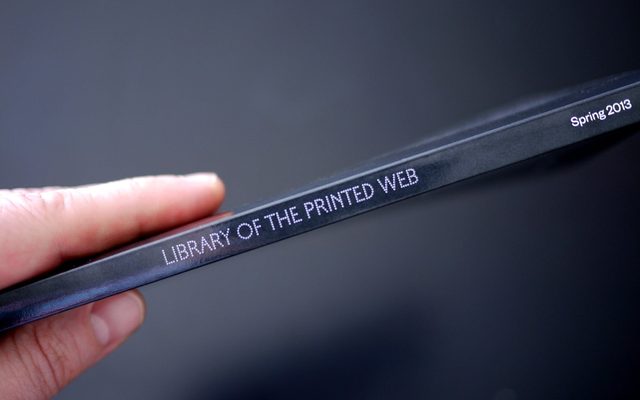 A fair skinned hand holding a thin book by the binding and it reads 