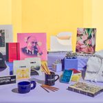 Display of Walker Art Center merchandise, including a hat, mugs, pencils, sweatshirt, notepads, books, sticjers and tiny gift boxes with silver bows.