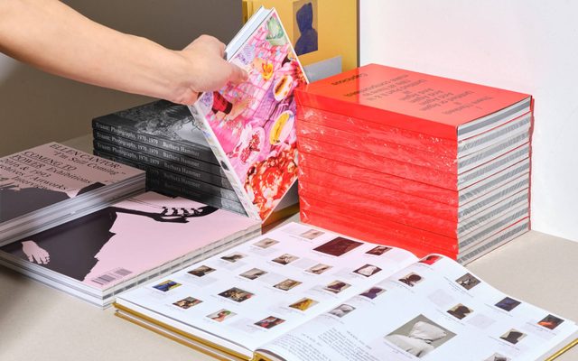 A neat grouping of books in various colors. A hand reaches to grab one.