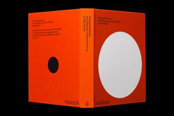 An orange book with a white circle on the front, standing upright on a black surface