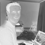 A negative-photo image of an adult smiling to the camera while on their laptop