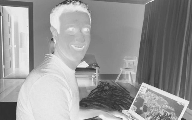 A negative-photo image of an adult smiling to the camera while on their laptop