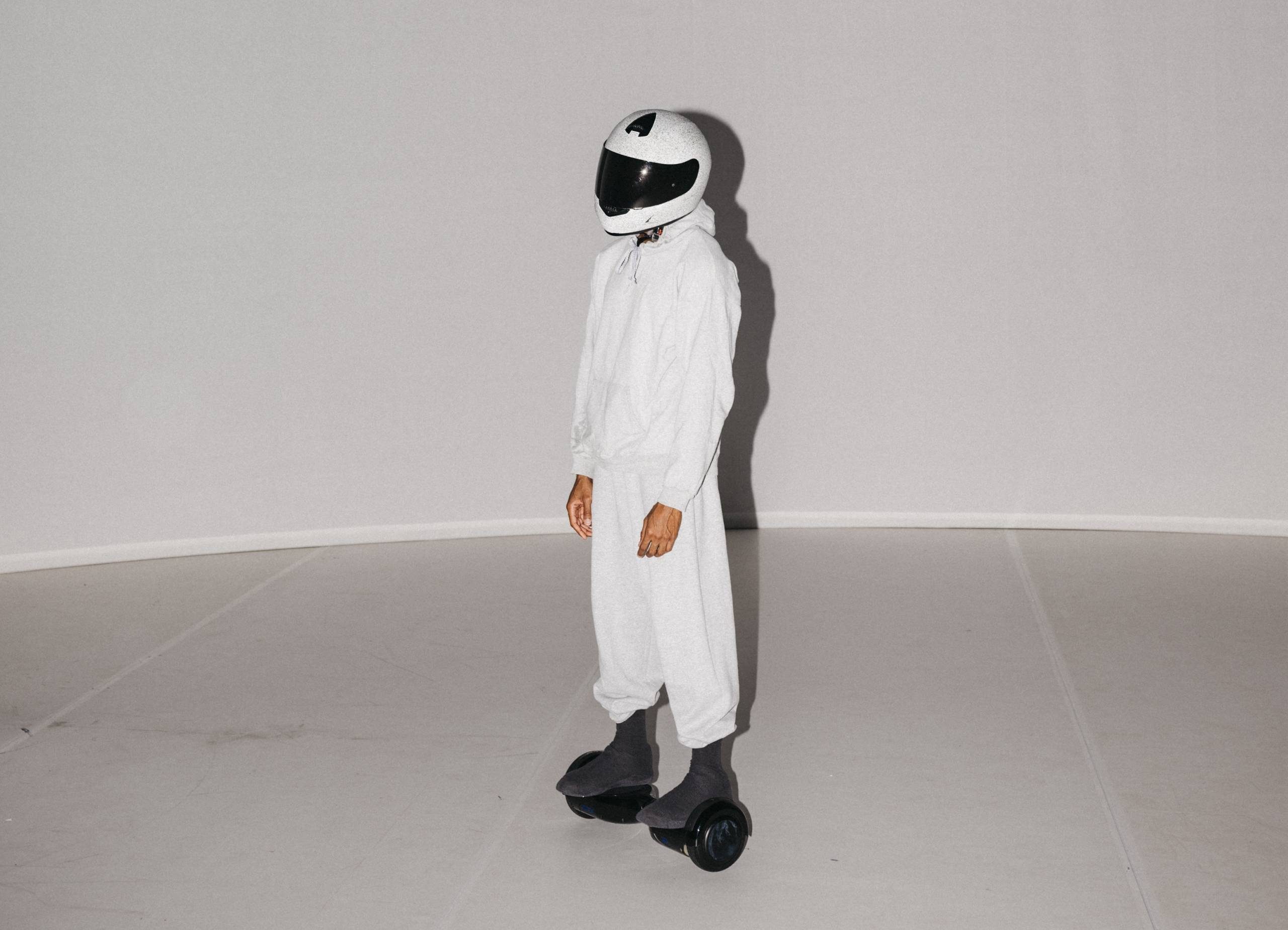 Person wearing an all white outfit and white helmet with black visor, standing on top of a helopad on wheels