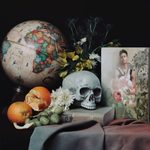 A display with an artists photo, globe, skull, book, flowers and unpeeled oranges on top of a table with a gray table cover.