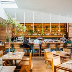 A restaurant with tables and chairs, and a long bar top with patrons sitting in bar stools and staff behind the bar.