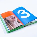 a colorful book open to a picture of a person with their mouth speaking and eyes covered by an orange rectangle next to a blue page with a large white number 