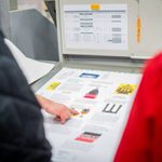 A hand pointing to a printed sample on a table