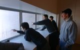 Four adults look and point out of a window during the day time