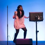 ex2015ipop_opn_121 A singer dances on stage with a microphone and a monitor in front of a blue background
