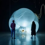 Two adults looking at a large illuminated and inflated art installation in a dark room