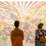 A view from behind two adults looking at a wall sized art map