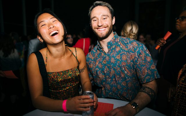 Two young adults posing for a photo, wearing event bracelets and holding a beverage, at a night event at the Walker Art Center
