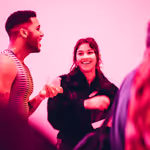 Two adults laughing in a gallery space that is lit pink