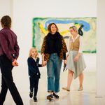 An adult holding an adolescents hand while walking through a museum with other visitors walking around.