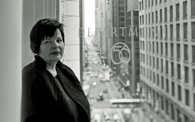 A black and white photo of woman standing next to a window with the logo: Department 56