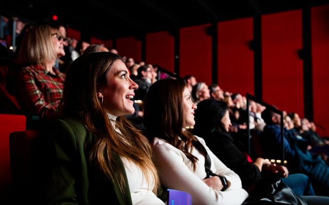 People sitting in the theatre audience looking towards a lit area