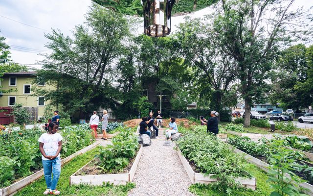 Adults and chidren explore an outdoors community garden art project during a sunny day.