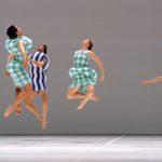 wac_13244 3 dancers jumping in place and one dancer posed on stage wearing green plaid and blue striped garments