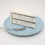 An art piece of a sliced white cake filled with two cut books that show the binding and pages, atop of a blue porcelain plate next to a fork