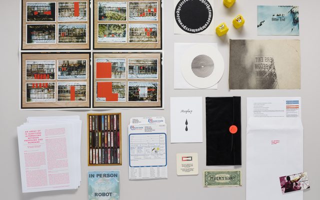 Spread out on display: historical images, printed material in red ink, tiny Spongebob smiley faces, a photo order envelope, a dollar bill, stickers, and envelopes