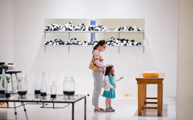 A woman and a girl stand in front of artwork in a gallery.