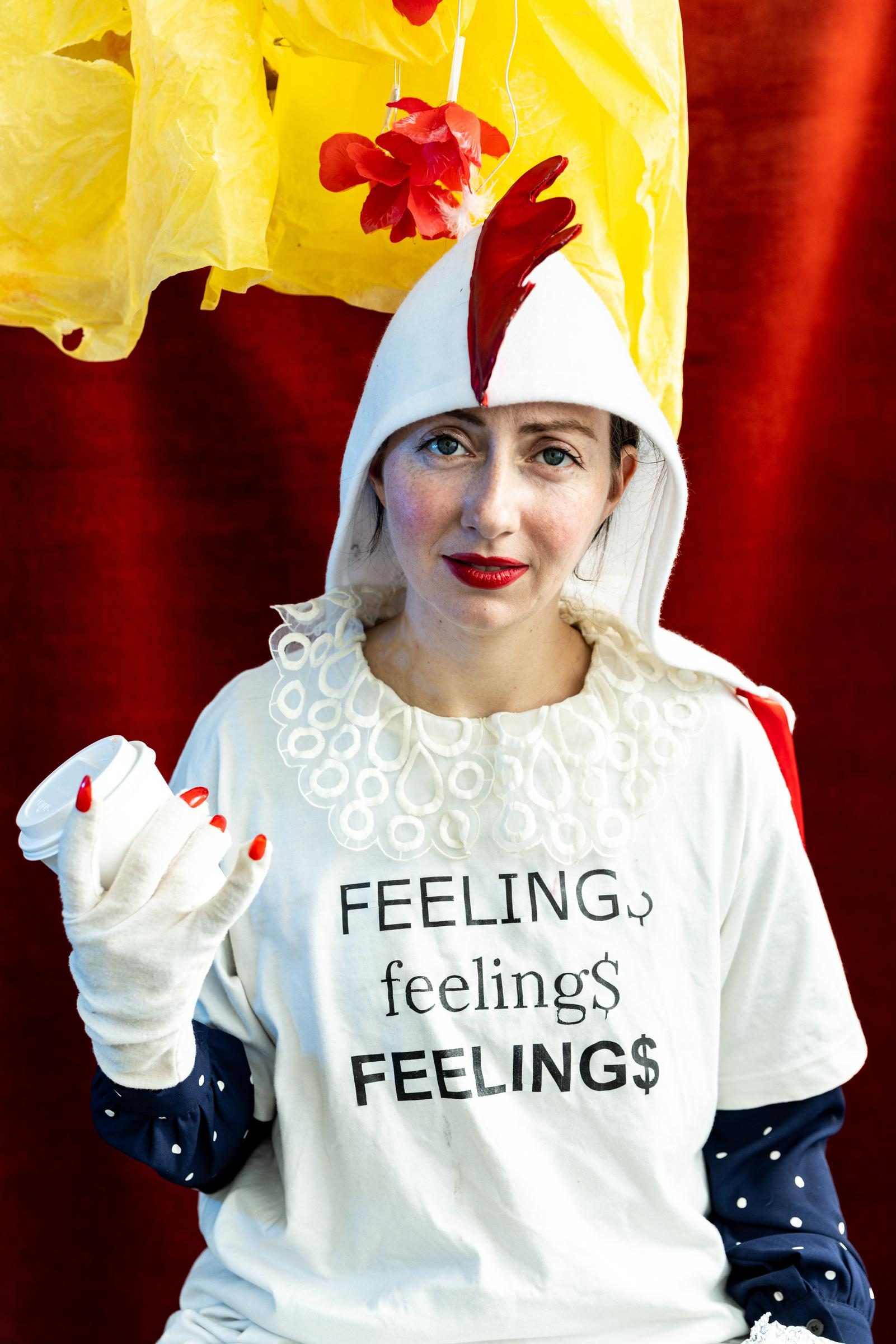 A performer with light skin poses with a coffee cup, a shirt that reads 