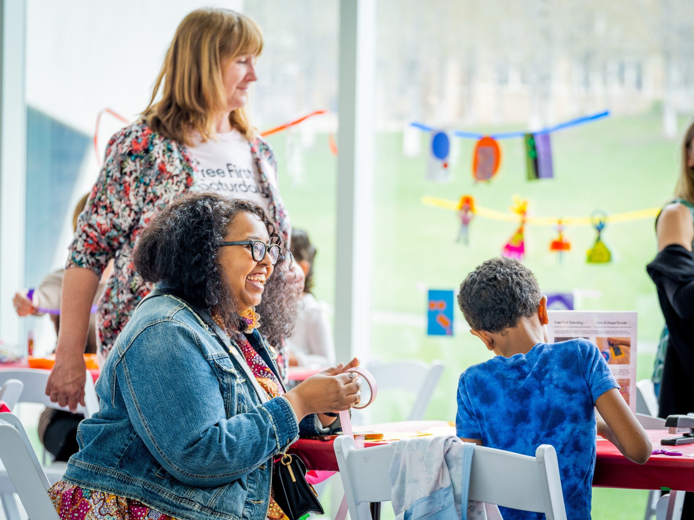 Two adults smile at a child working on an art project. 